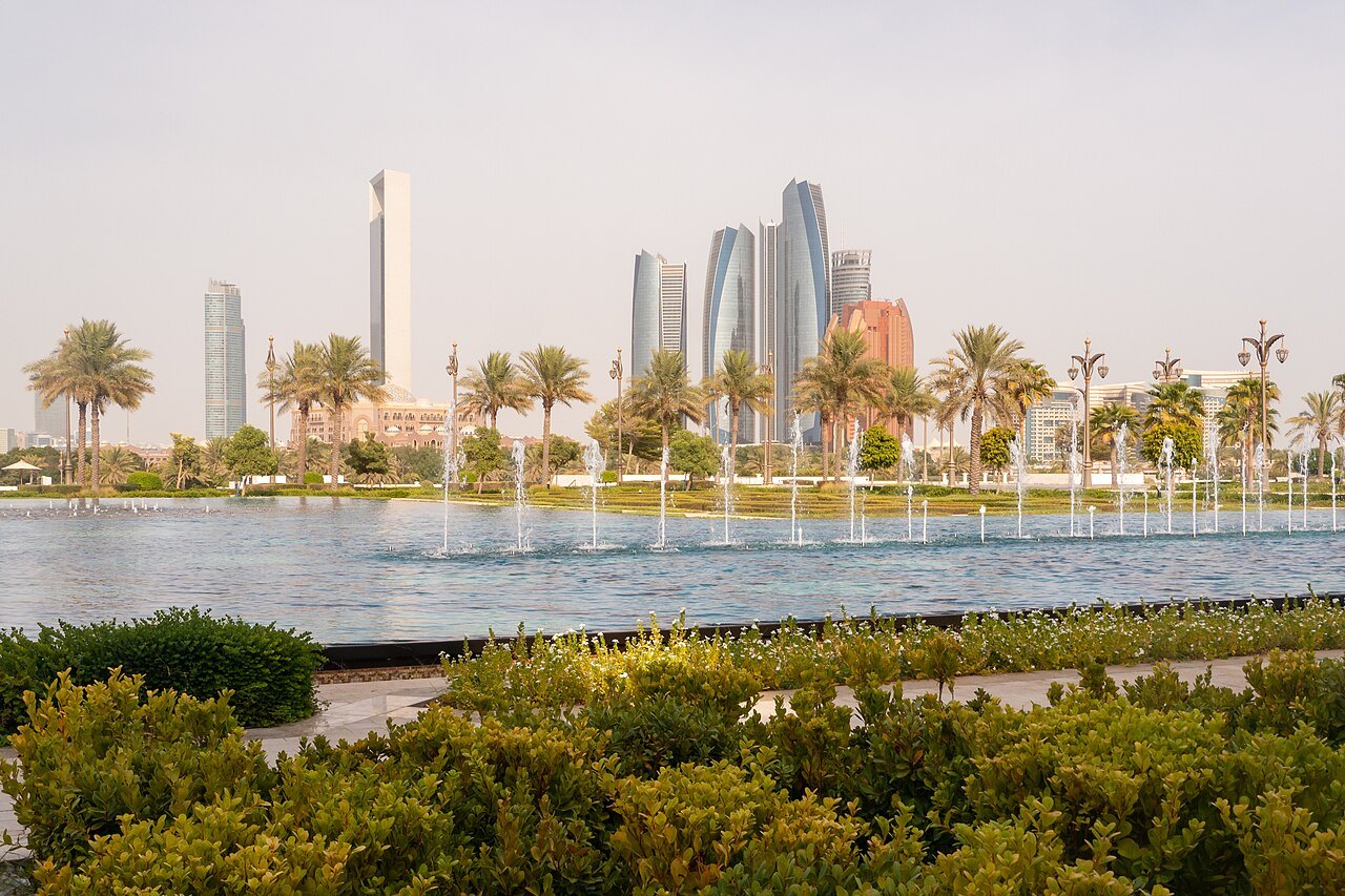 Fountains and palm trees in the gardens of Qasr Al Watan with Abu Dhabi's towers on the skyline behind