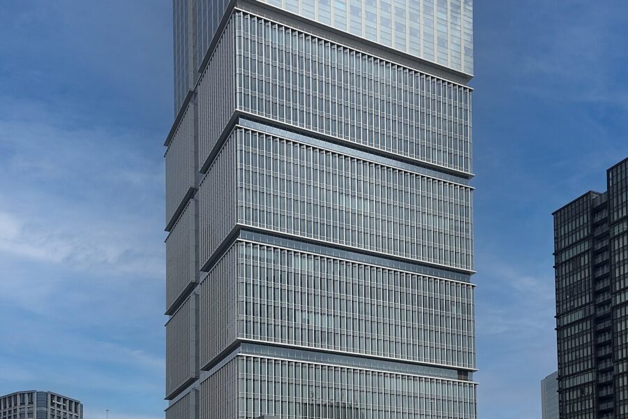 A tall glass and stone office tower rising above a tree-lined plaza in central Tokyo.