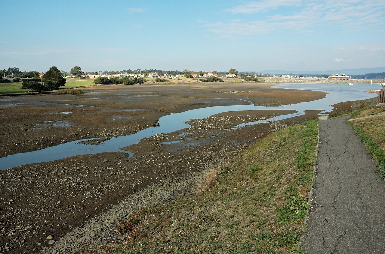 A sheltered cove with moored boats and low buildings on the far shore, seen on a clear day in northern Tasmania.