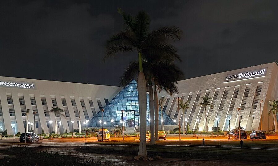 A low-rise glass and stone office building lit from below at dusk, set behind planted grounds.