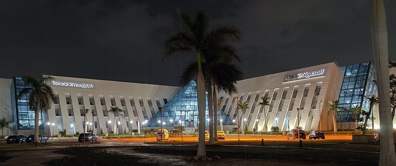 A low-rise glass and stone office building lit from below at dusk, set behind planted grounds.