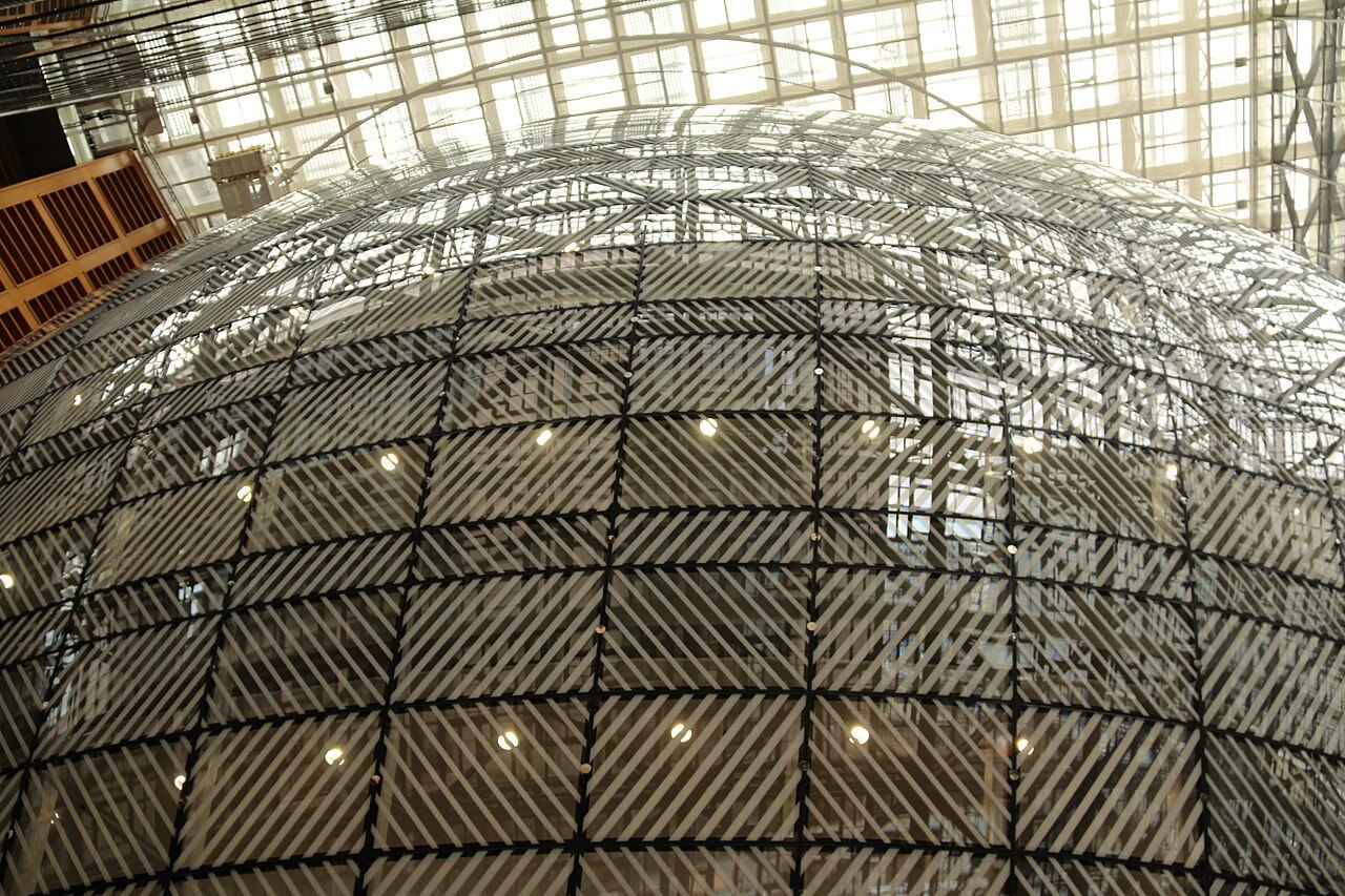 Interior view of the glass lantern structure inside the Europa building in Brussels, with a curved, striped glass shell under a glazed atrium roof