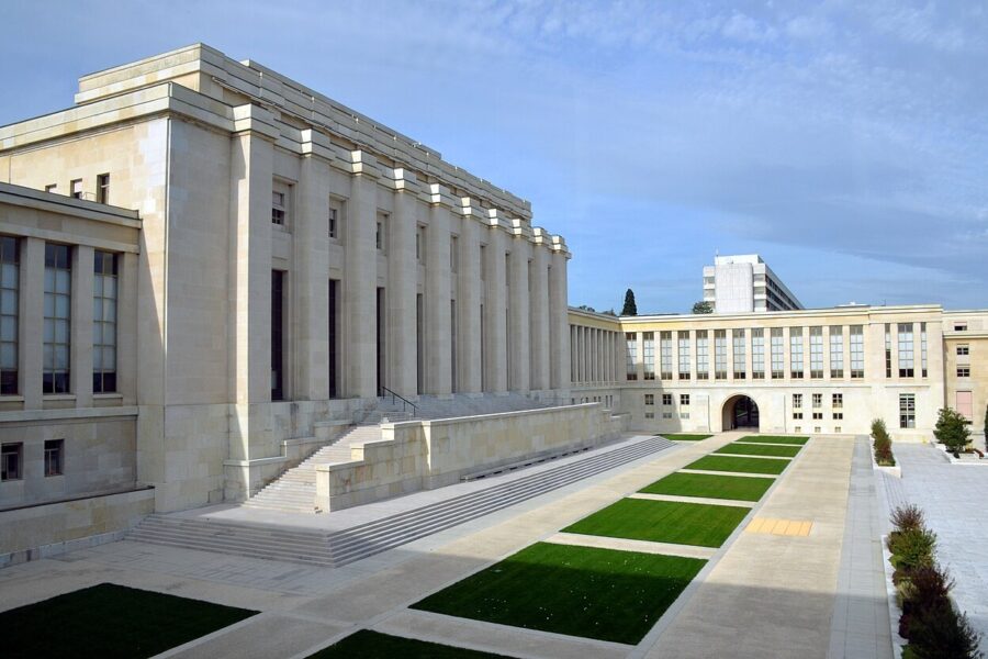 The long colonnaded facade of the Palais des Nations in Geneva seen from the lawns in front of it.