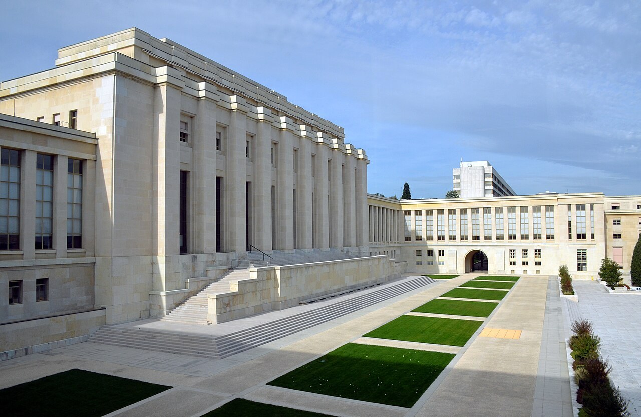 The long colonnaded facade of the Palais des Nations in Geneva seen from the lawns in front of it.