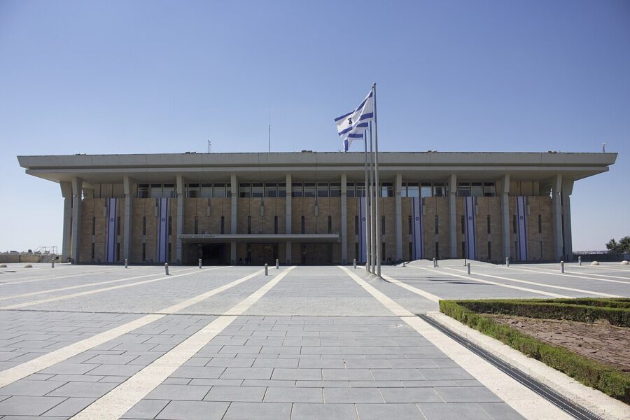 The front elevation of the Knesset building in Jerusalem, a flat-roofed stone and concrete parliament set behind an open forecourt.