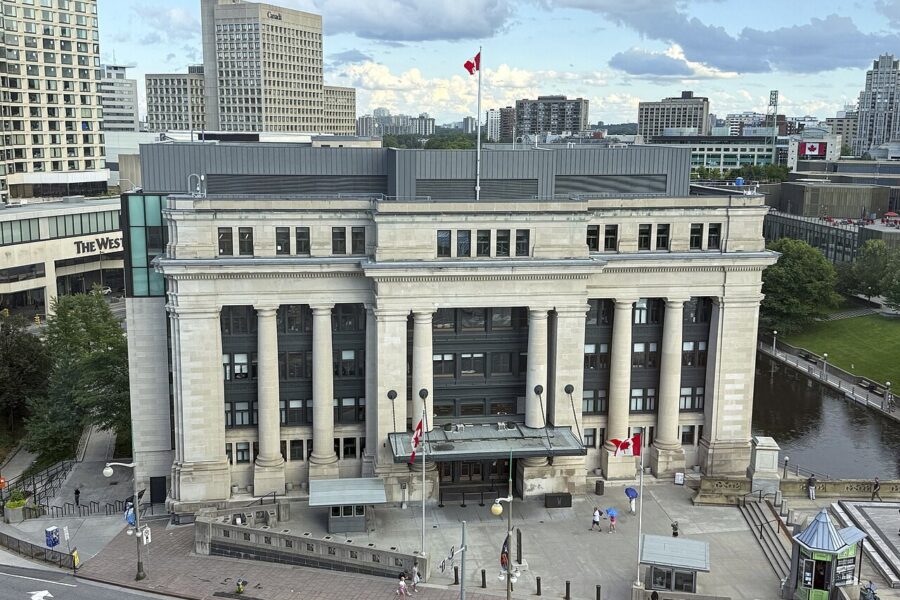 A stone neoclassical building with a tall colonnade across its front, seen from above beside a canal in central Ottawa.