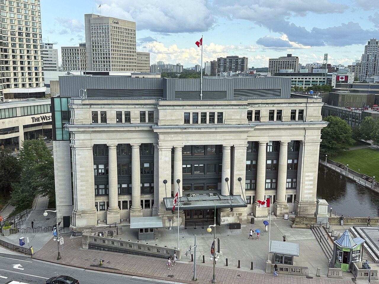 A stone neoclassical building with a tall colonnade across its front, seen from above beside a canal in central Ottawa.