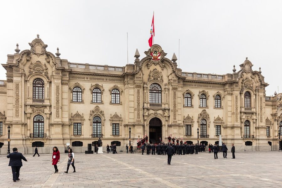 The facade of the Government Palace in Lima seen across the square in front of it under a pale sky.