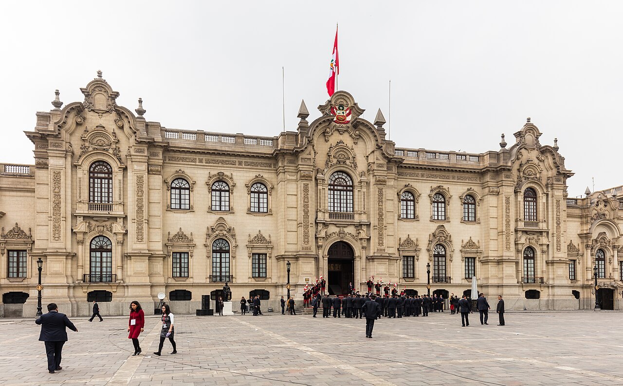 The facade of the Government Palace in Lima seen across the square in front of it under a pale sky.