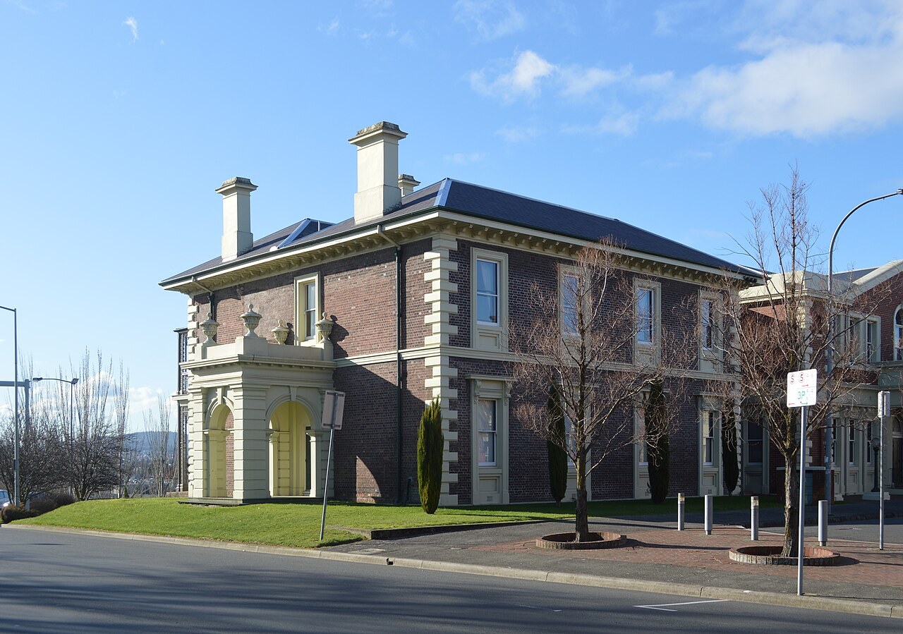 A two-storey nineteenth-century brick and stone courthouse on a street corner under a clear blue sky.